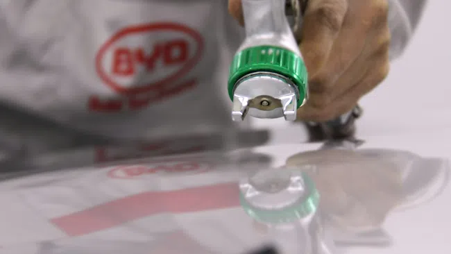 Worker using a spray gun for painting or coating on a reflective surface with BYD logo on uniform