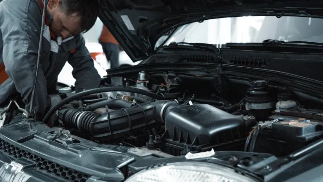 Mechanic inspecting and repairing a car engine under the raised hood in a garage workshop environment