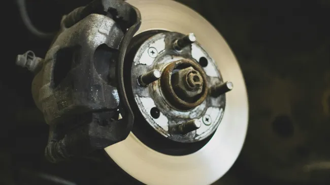 Close-up of a car brake rotor and caliper with metallic and rust details in a dark setting