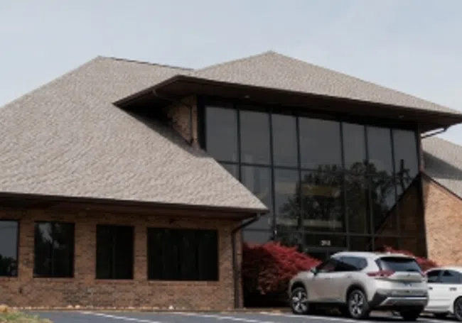 Modern brick office building with large glass windows and cars parked in front on a clear day..
