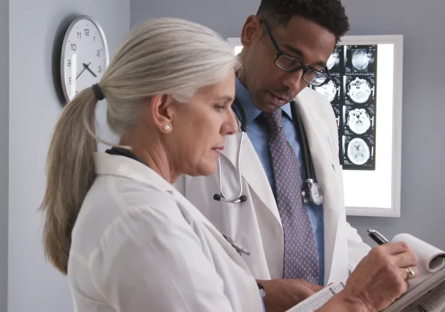two doctors reviewing notes in front of a medical scan.