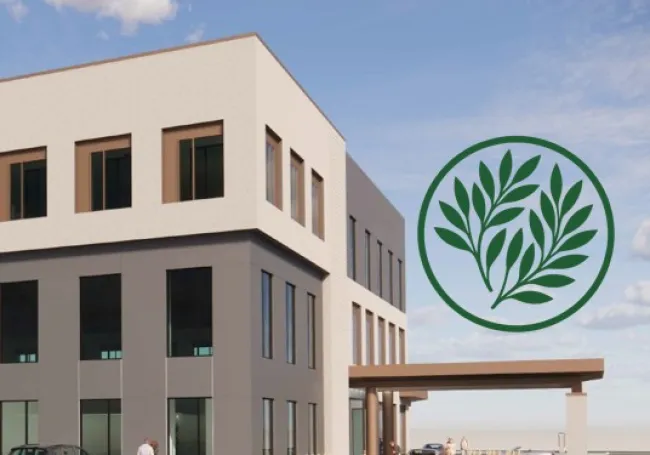 Modern two-story building with large windows and a green leafy logo on the side under a cloudy sky..