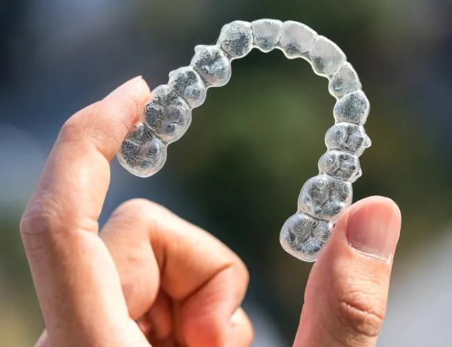 Hand holding a clear dental aligner used for orthodontic teeth straightening against a blurred background