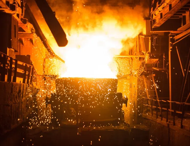 Molten metal pouring in a foundry with bright flames and flying sparks creating an intense industrial scene.