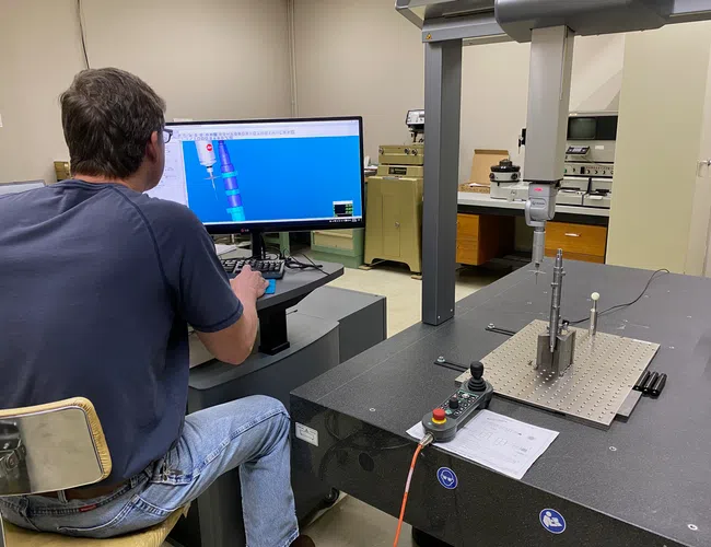 Man operating precision measurement machine with CAD model displayed on computer screen in lab setting.