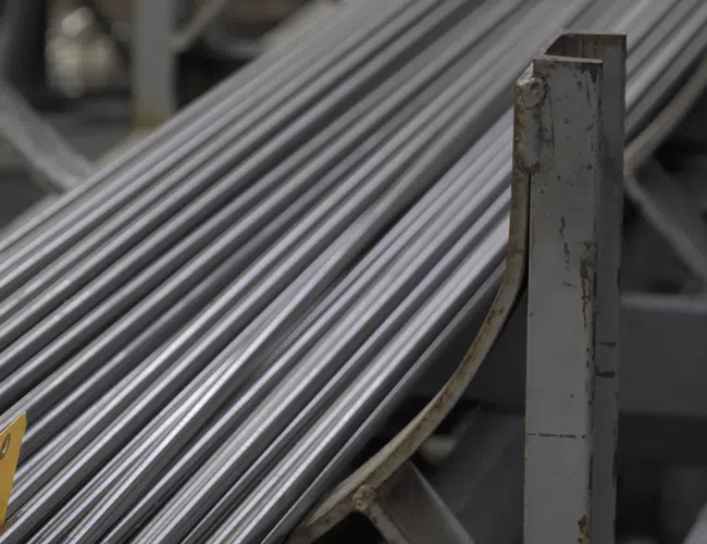 Stack of long, polished metal rods arranged on industrial racks in a factory setting.