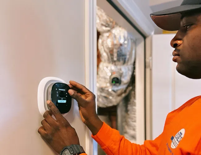 A Estes technician adjusting a smart thermostat on a wall in a modern home.