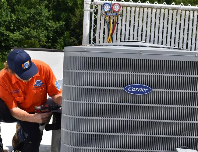 Estes Technician servicing a Carrier air conditioning unit on a rooftop with tools in hand.