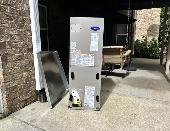 Carrier HVAC unit standing outdoors on concrete near brick wall and patio swing.