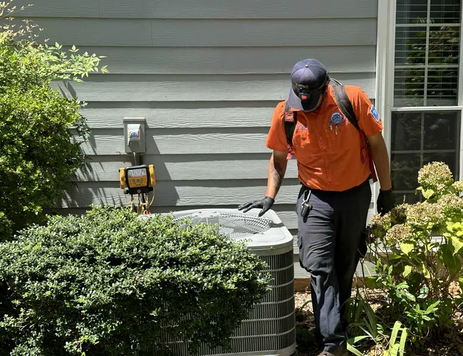 Estes Technician inspecting an outdoor air conditioning unit next to a house during a maintenance check on a sunny day