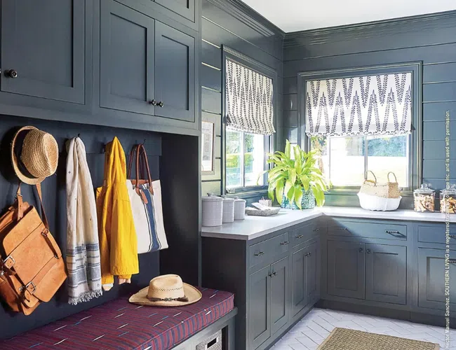 Modern mudroom with gray cabinetry, bench seating, woven baskets, hats, bags, and natural light through windows.