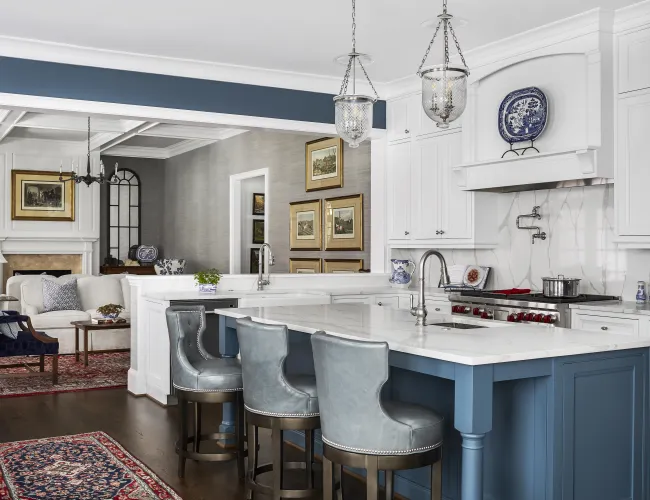 Modern kitchen with white cabinets, blue island, marble countertop, and adjacent living area with fireplace and rugs.