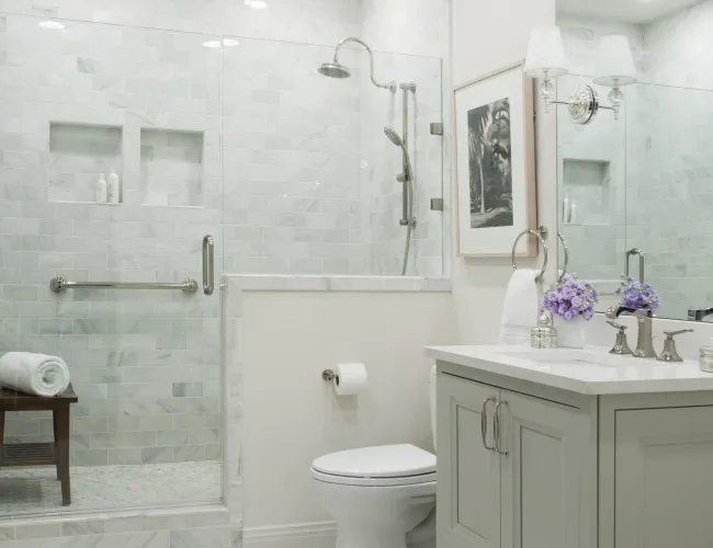 Bright modern bathroom with glass shower, white vanity, toilet, and decorative purple flowers on the counter