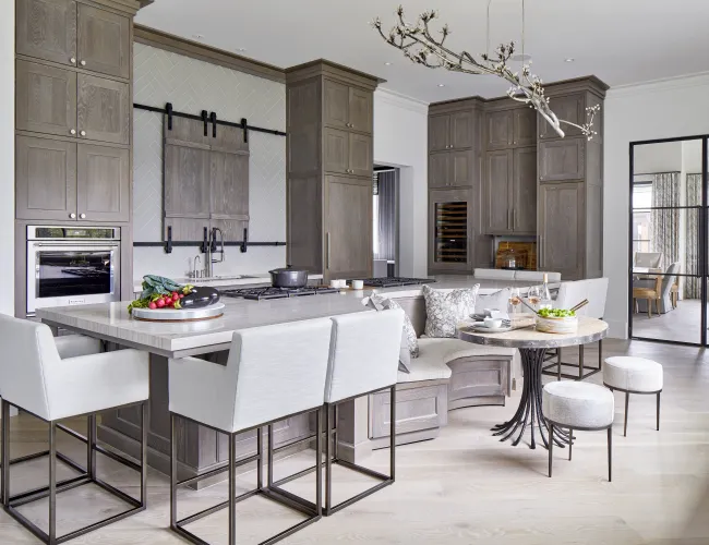 Modern kitchen with gray cabinetry, white island with seating, built-in oven, and unique branch chandelier.
