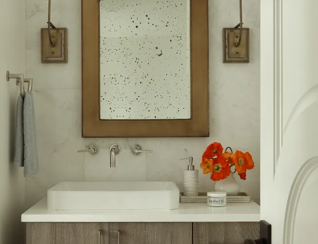 Modern bathroom vanity with unique bronze-framed mirror, wall sconces, and wood cabinets with floral decor.