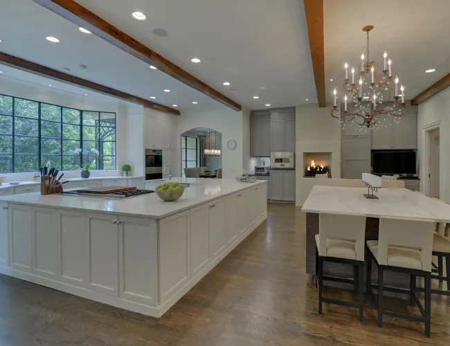 Spacious modern kitchen with large white island, hardwood floors, chandelier, and large black-framed windows.