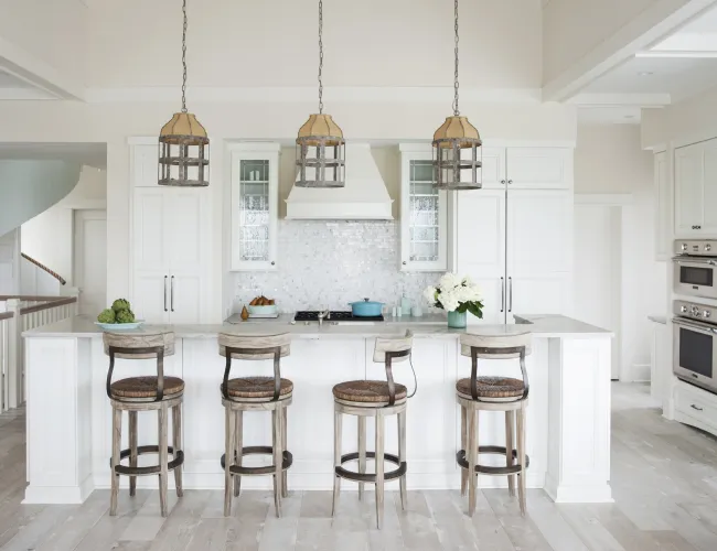 Bright white kitchen with island seating, wooden bar stools, pendant lights, and stainless steel appliances.