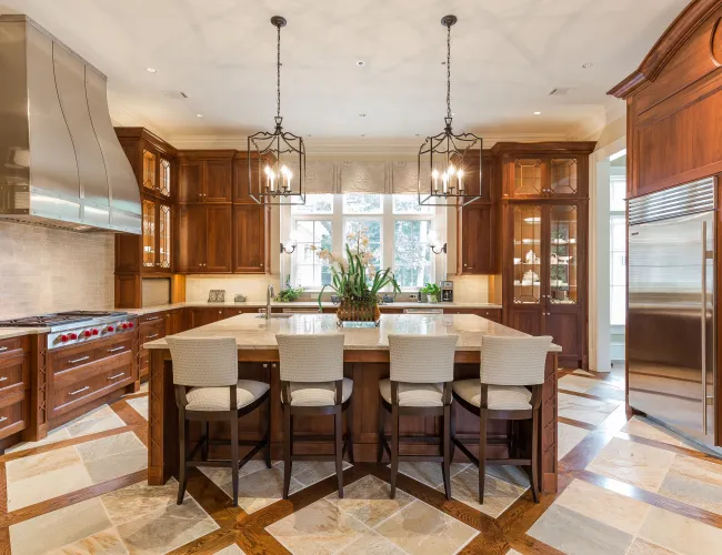 Spacious kitchen with wooden cabinets, stainless steel appliances, island with four chairs, and pendant lights.