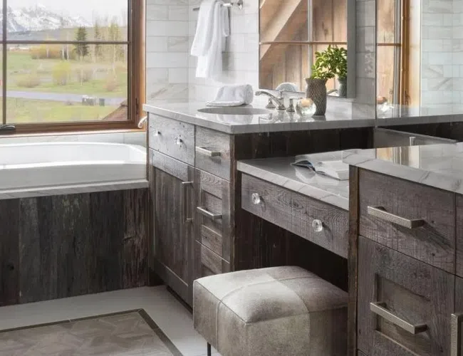 Modern bathroom with dark wood cabinetry, gray stool, marble countertops, large mirror, and window with mountain view.