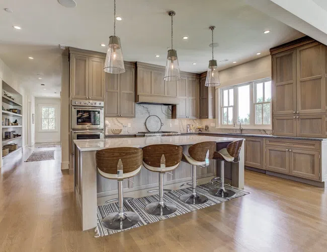 Modern kitchen with wood cabinetry, marble countertops, four bar stools, pendant lights, and hardwood floors