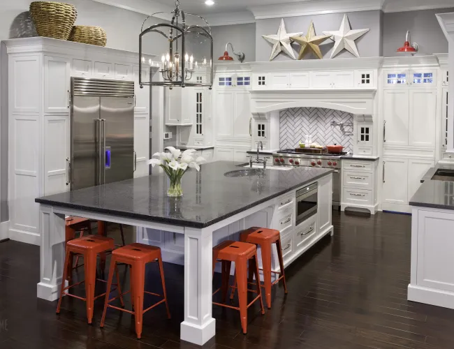 Modern white kitchen with large black granite island, orange stools, stainless steel appliances, and star wall decor.