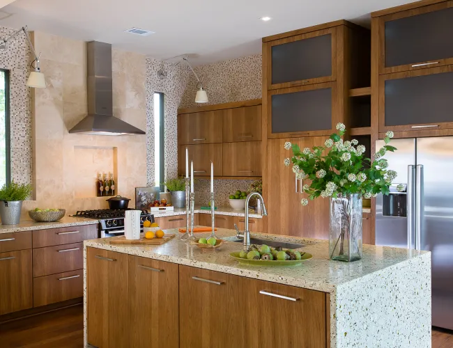 Modern kitchen with wood cabinets, terrazzo countertops, stainless steel appliances, and decorative plants.