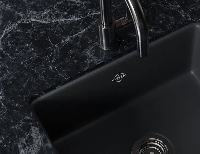 Modern black kitchen sink with stainless steel faucet installed in a dark marble countertop.