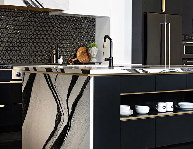 Modern kitchen with black and white marble island, matte black cabinets, geometric backsplash, and gold accents.