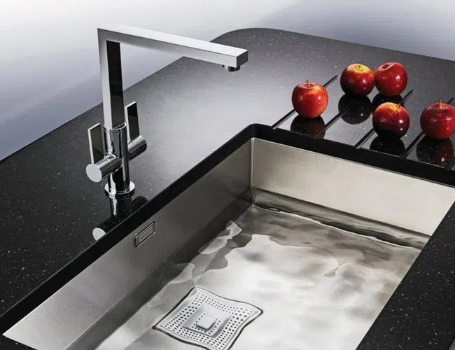 Modern kitchen sink with sleek chrome faucet on black granite countertop with four red apples.