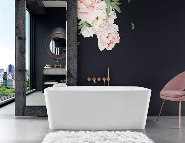 Modern bathroom with white freestanding tub, large mirror, pink chair, floral wall decal, and city skyline view.