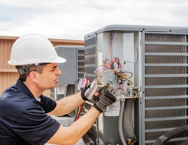 Technician wearing hard hat and gloves repairing an outdoor air conditioning unit on a rooftop