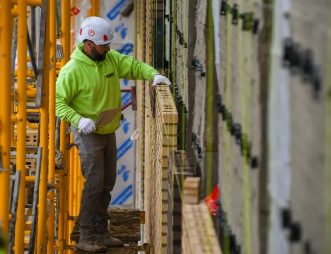 Construction worker in safety gear installing brickwork on scaffolding at building site