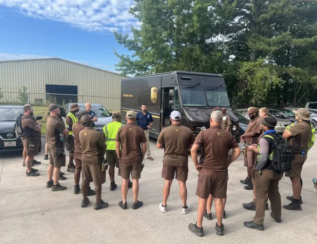UPS delivery team gathered outdoors for a meeting near brown delivery truck on a sunny day
