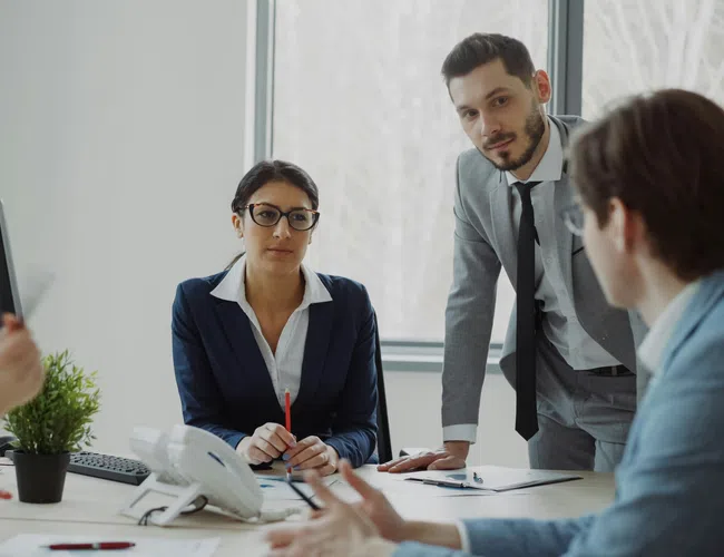 Business team in formal attire engaged in a discussion around a conference table in a modern office.