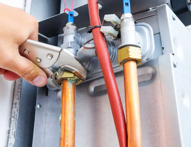 Hand tightening a pipe fitting on copper plumbing with an adjustable wrench, surrounded by pipes and valves