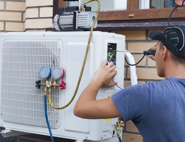 Technician repairing an air conditioning unit on a brick wall, showcasing tools and gauges.