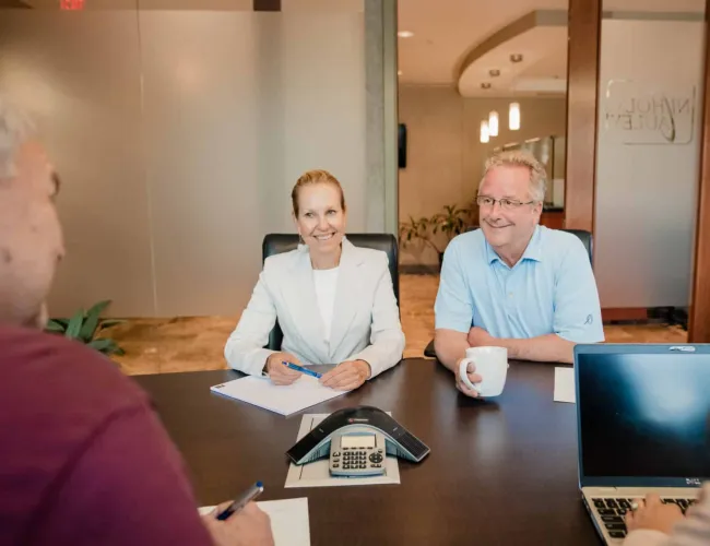 Business meeting with four professionals discussing around a conference table with laptop and speakerphone.