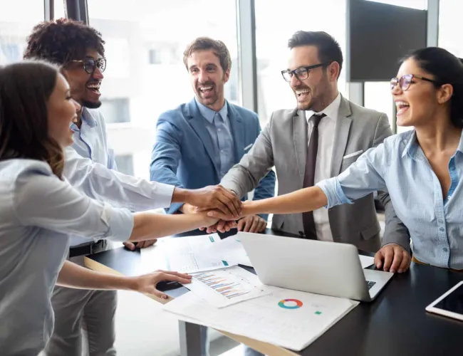 Diverse business team joining hands in office meeting for teamwork and success with charts and laptop