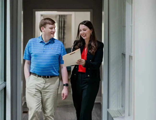 Two colleagues walking down a hallway discussing documents with smiles in a professional office setting