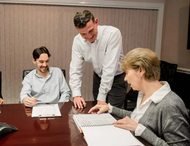 Three coworkers engaged in a meeting, reviewing documents around a conference table with smiles and focus.