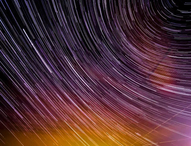 Long exposure of star trails creating circular light patterns over a colorful night sky.