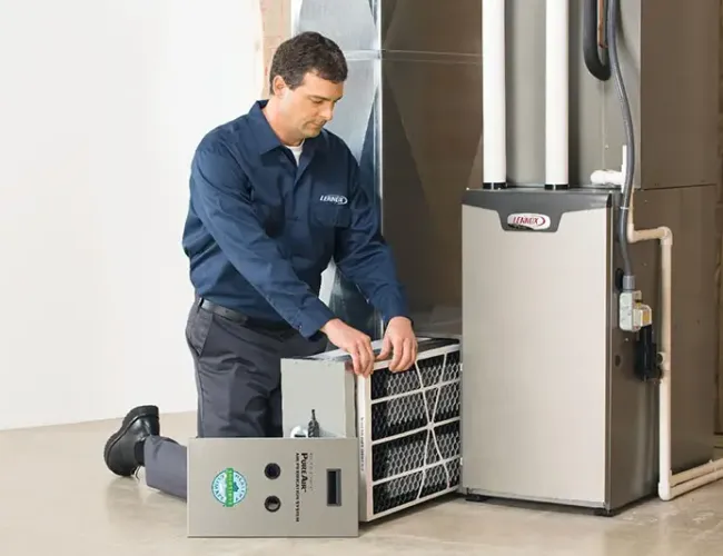 Technician in uniform installing or replacing an air filter in a home furnace system indoors.