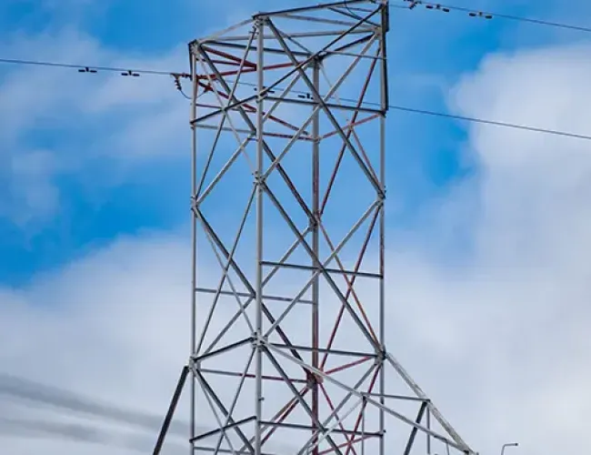 Steel lattice transmission tower supporting high voltage power lines against a partly cloudy blue sky.