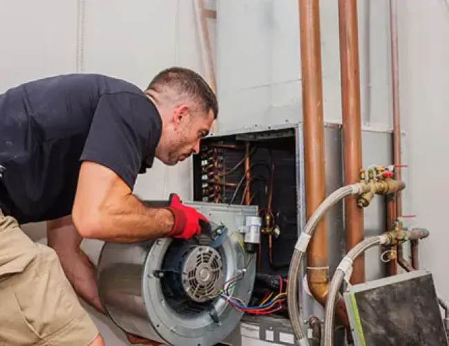 Technician repairing HVAC system blower motor with tools and copper piping in residential heating unit.