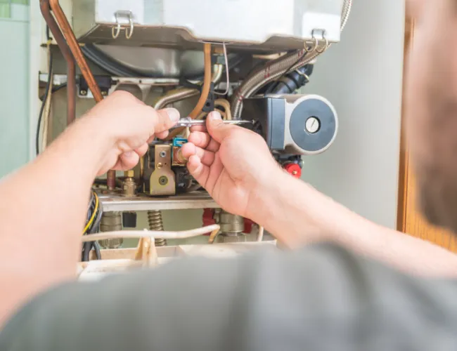 Technician repairing a boiler with a wrench, focusing on hands adjusting plumbing components inside the unit.