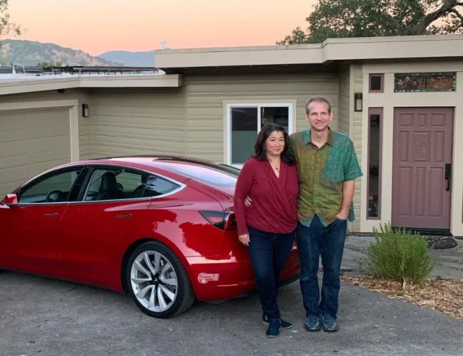 a man and woman standing next to a red car in front of a house