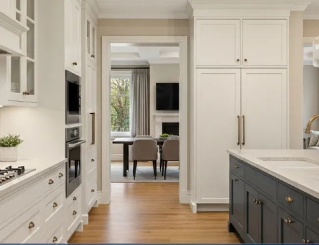 Modern kitchen with white cabinets, gray island, brass fixtures, gas stove, and view into dining room with fireplace