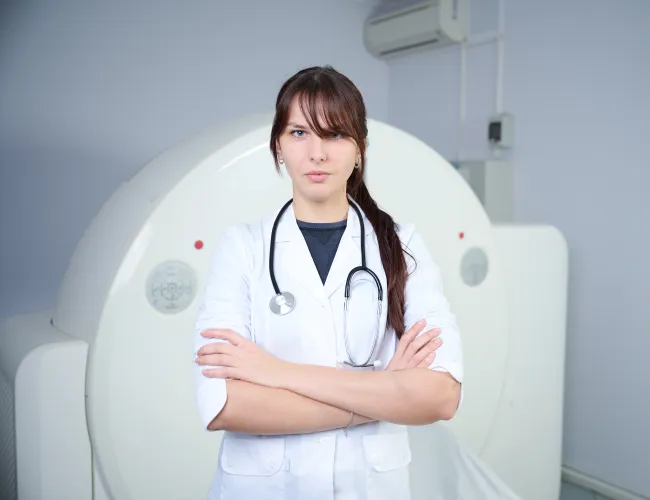 Confident female doctor standing with arms crossed in a medical imaging room.