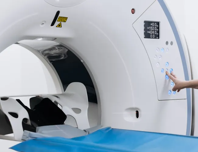Close-up of a CT scanner control panel with a hand pressing buttons for operation.