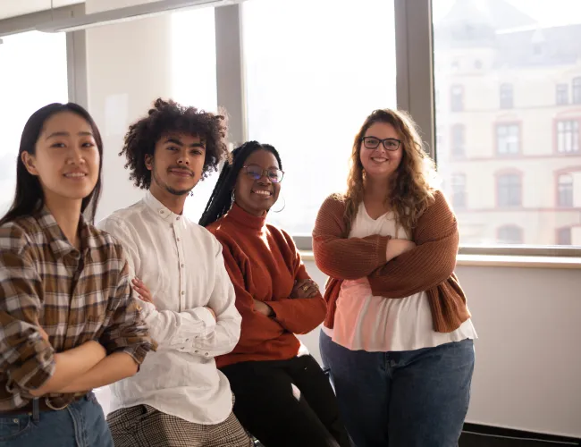 Diverse group of young professionals standing confidently with arms crossed in bright modern office.